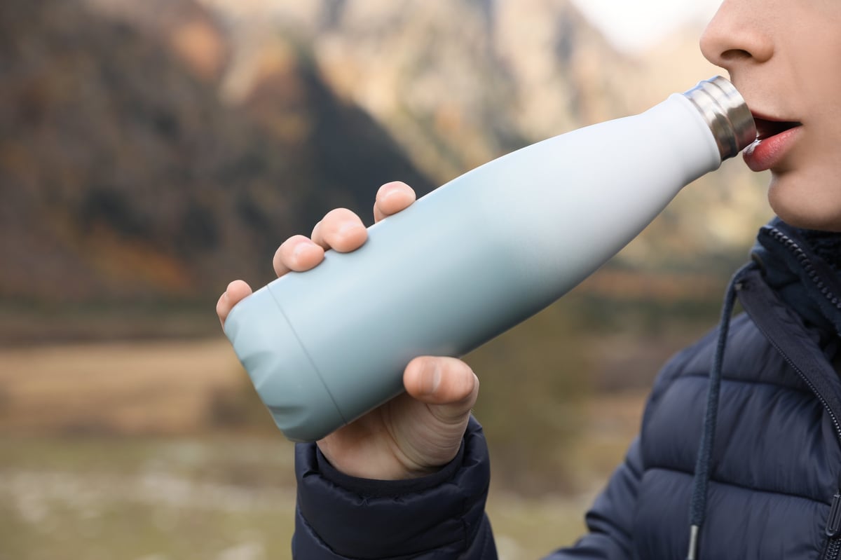 Person drinking from a branded water bottle outdoors
